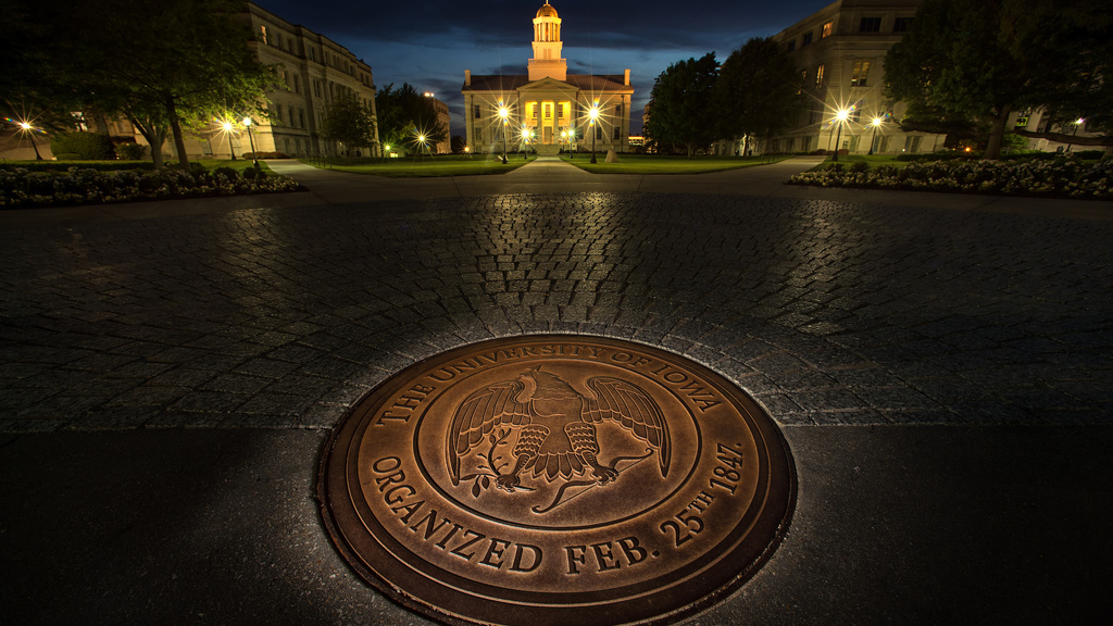 A view of the seal of the University of Iowa at night with the Old Capitol in the background